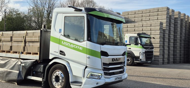 A white and green truck with concrete blocks stacked on its back and in the background
